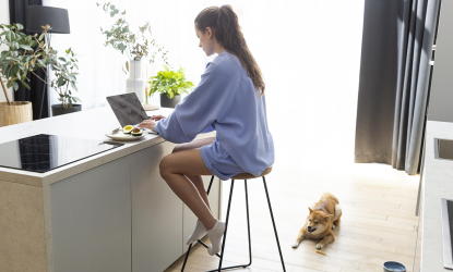 Žena sjedi za šankom u kuhinji i radi na laptopu.