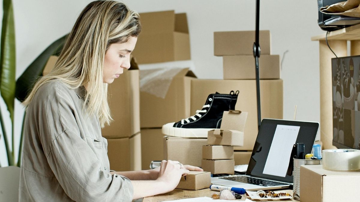 e-commerce, internet prodaja, online, zaposlenica radi na laptopu, oko nje kutije i tenisica