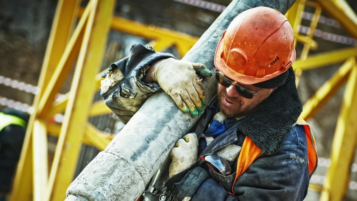 Radnik na građevini, građevinski radnik, građevinac, muškarac nosi stup Pexels